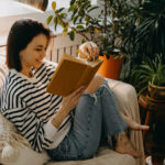 Frau sitzt auf der Couch und liest Feminismus-Bücher