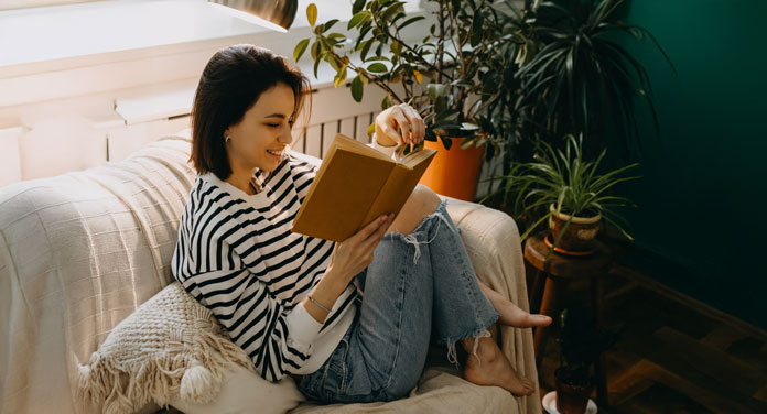 Frau sitzt auf der Couch und liest Feminismus-Bücher