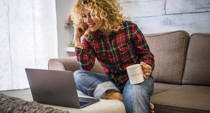 Frau betrachtet ihre Mind Movies auf dem Laptop mit einer Tasse Kaffee in der Hand