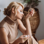 Parfum-Guide: Frau riecht an ihrem Handgelenk mit einem Parfum-Flakon in der anderen Hand