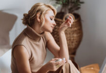 Parfum-Guide: Frau riecht an ihrem Handgelenk mit einem Parfum-Flakon in der anderen Hand