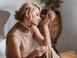 Parfum-Guide: Frau riecht an ihrem Handgelenk mit einem Parfum-Flakon in der anderen Hand