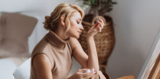 Parfum-Guide: Frau riecht an ihrem Handgelenk mit einem Parfum-Flakon in der anderen Hand