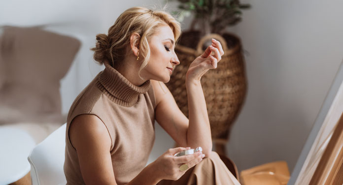Parfum-Guide: Frau riecht an ihrem Handgelenk mit einem Parfum-Flakon in der anderen Hand