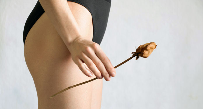Frau im Slip mit getrockneter Rose in der Hand als Symbol für Scheidentrockenheit