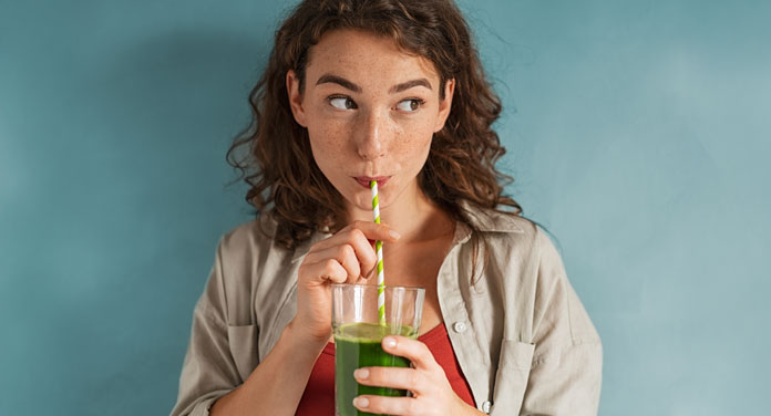 Frau trinkt einen grünen Smoothie aus einem Strohhalm mit Proteinpulver von HANS Brainfood