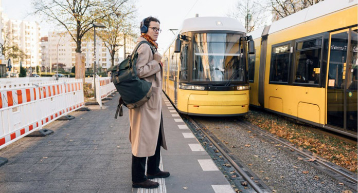 Mann mit Rucksack im Mantel steht an der Straßenbahn-Haltestelle