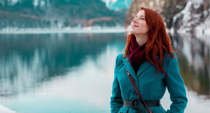 Frau im blauen Mantel atmet im Winter draußen am See tief ein