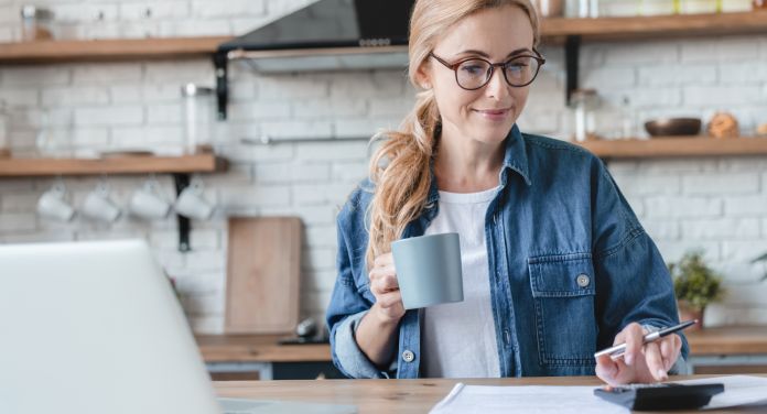 Frau arbeitet am Schreibtisch mit Taschenrechner - Psychologie des Geldes