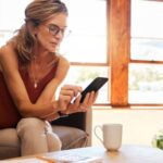 Frau nutzt Smartphone auf der Couch - Versicherungen für Frauen
