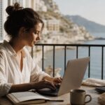 Frau arbeitet mit Laptop auf einem Balkon mit Meerblick